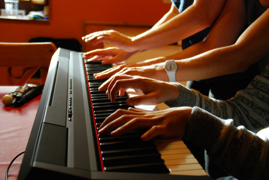 drei Paar Hände spielen auf einer Klaviatur