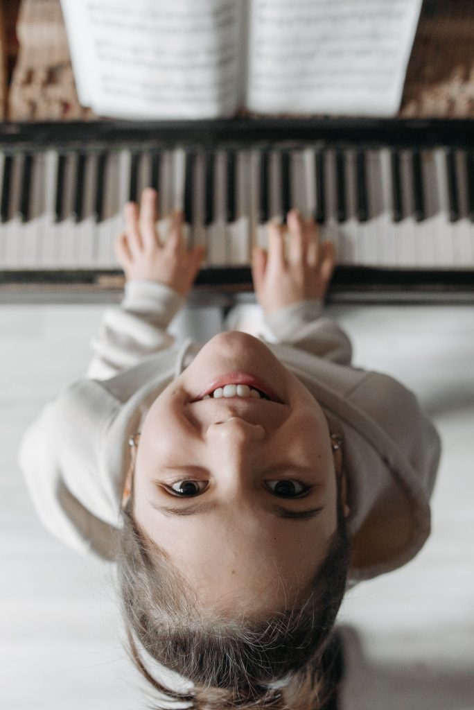 Ein Mädchen sitzt lächelnd am Klavier. Klavierunterricht bedeutet erst einmal Kosten
