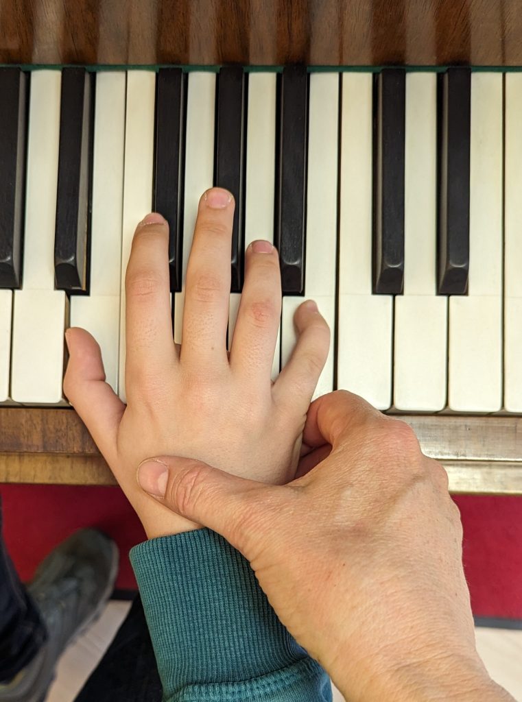 Die Hand der Klavierlehrerin führt die Hand des Schülers im Klavierunterricht