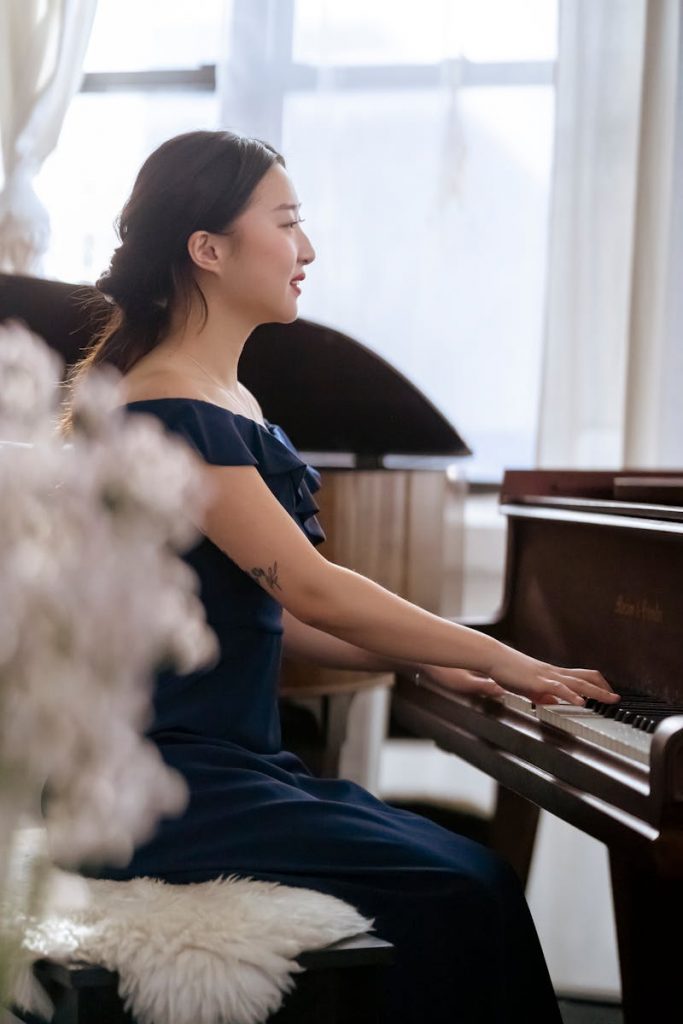 Side view of ethnic woman in elegant dress sitting on chair and playing piano 